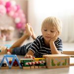 cute child, blond toddler boy, playing with wooden trains at hom