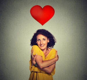 portrait smiling woman holding hugging herself with red heart above head