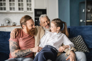 LGBTQ parents with daughter sitting on their lap. Everyone is laughing and appear happy.