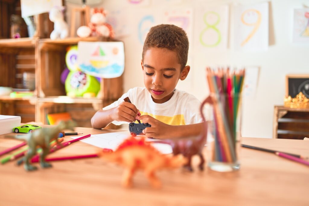 child sitting painting car toy using marker pen on desk in therapeutic playroom